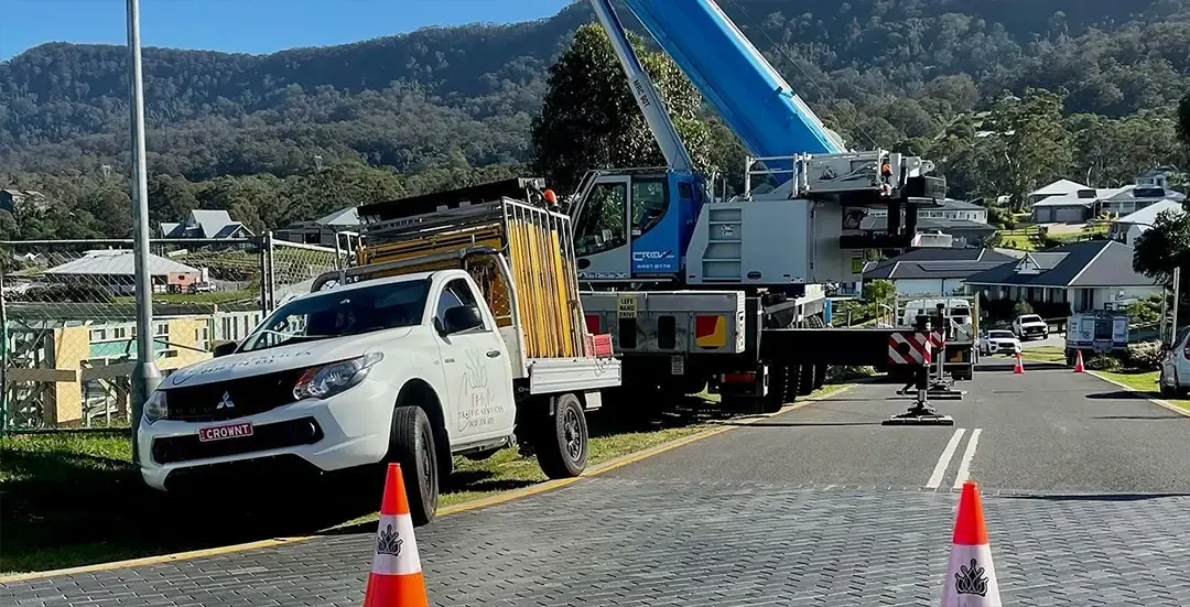 A Crown ute and cones beside a crane lift on a residential street