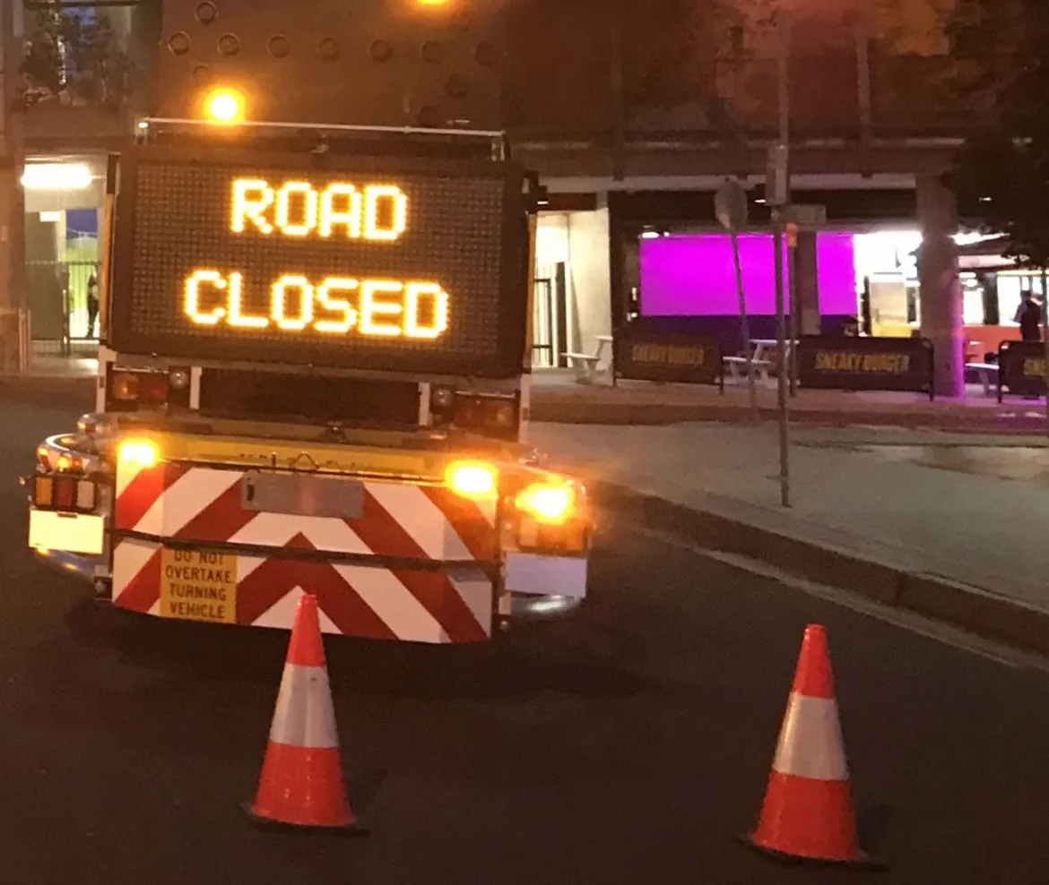 A road closed sign and message board at night